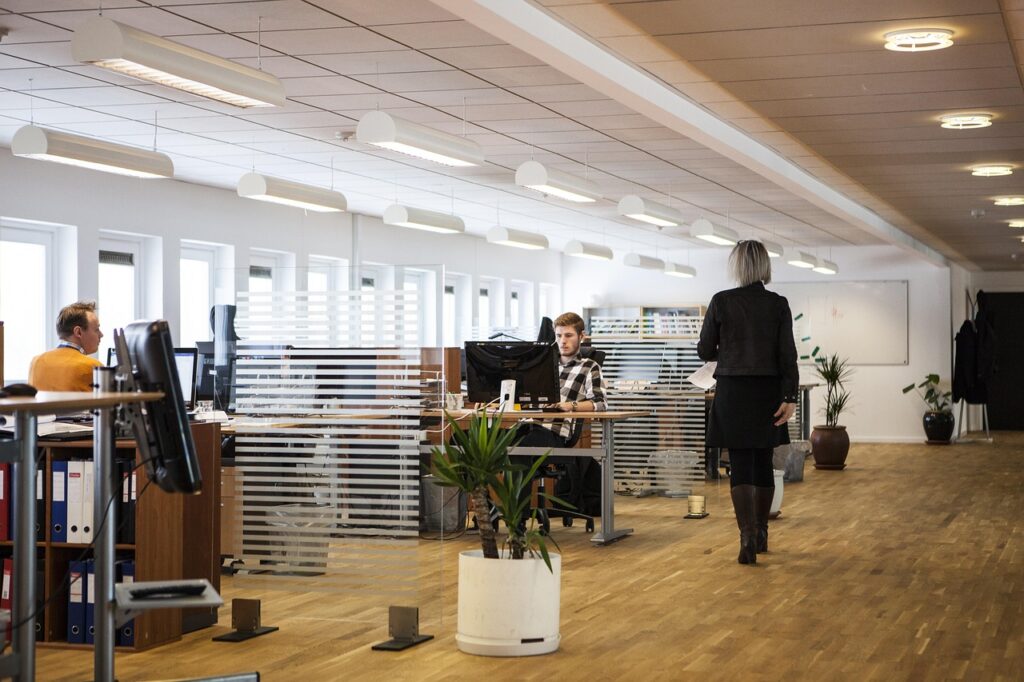 Moderne Büroszene mit Mitarbeitenden bei der Arbeit und einer Frau im Gespräch – Symbol für erfolgreiche HR-Reintegration und Zusammenarbeit im Unternehmen.