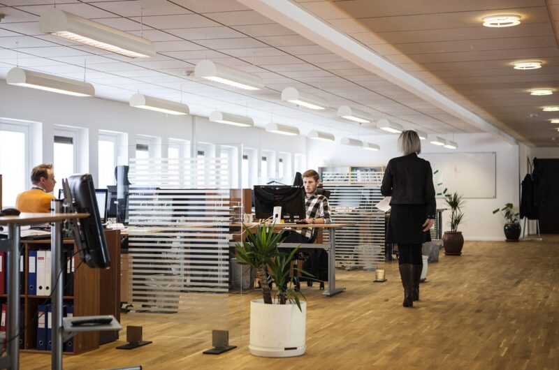 Moderne Büroszene mit Mitarbeitenden bei der Arbeit und einer Frau im Gespräch – Symbol für erfolgreiche HR-Reintegration und Zusammenarbeit im Unternehmen.